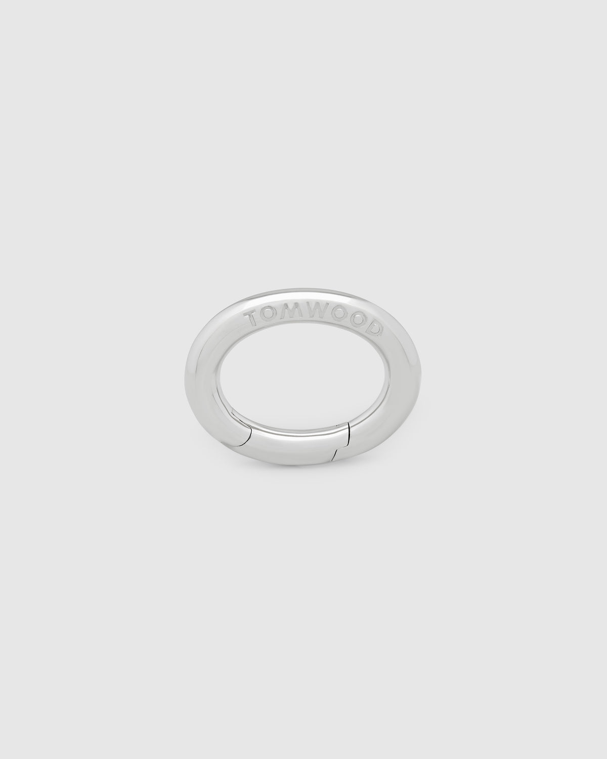 A silver metal key clasp with a flat, circular design and the brand name 'TOMWOOD' engraved on the top, set against a solid light gray background.