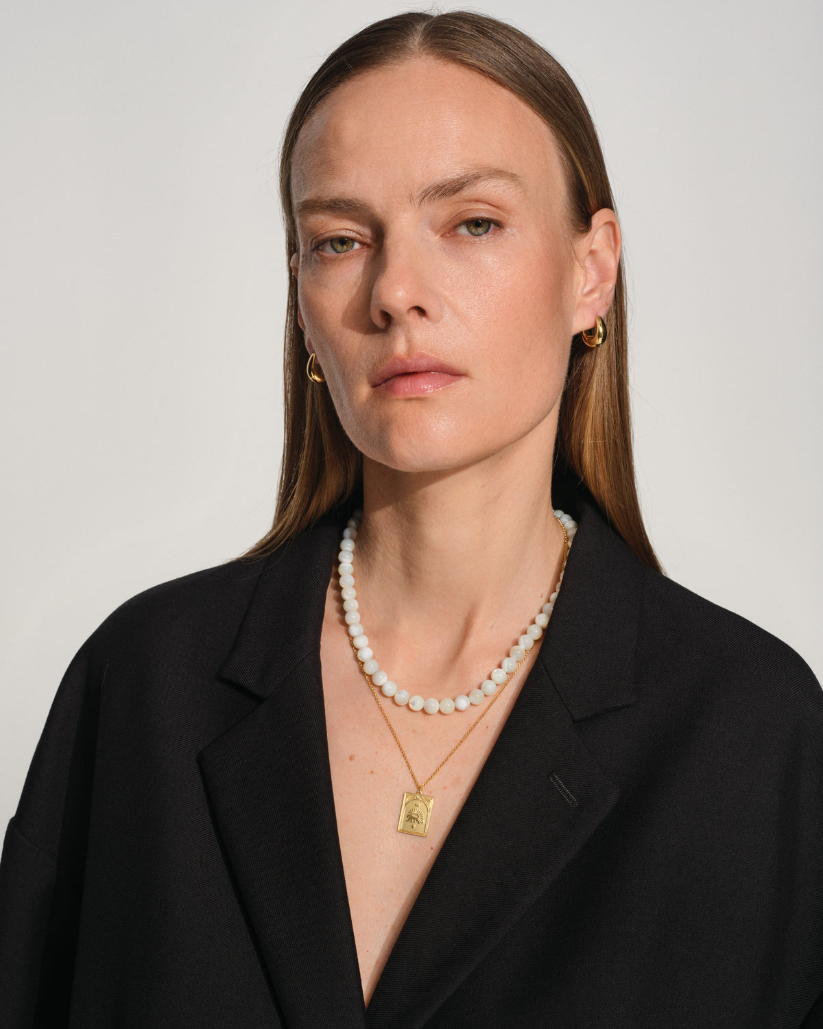 Tom Wood Cove Necklace White MOP - Woman wearing layered jewelry, including a double-strand white pearl necklace and a gold pendant necklace, along with small gold hoop earrings.