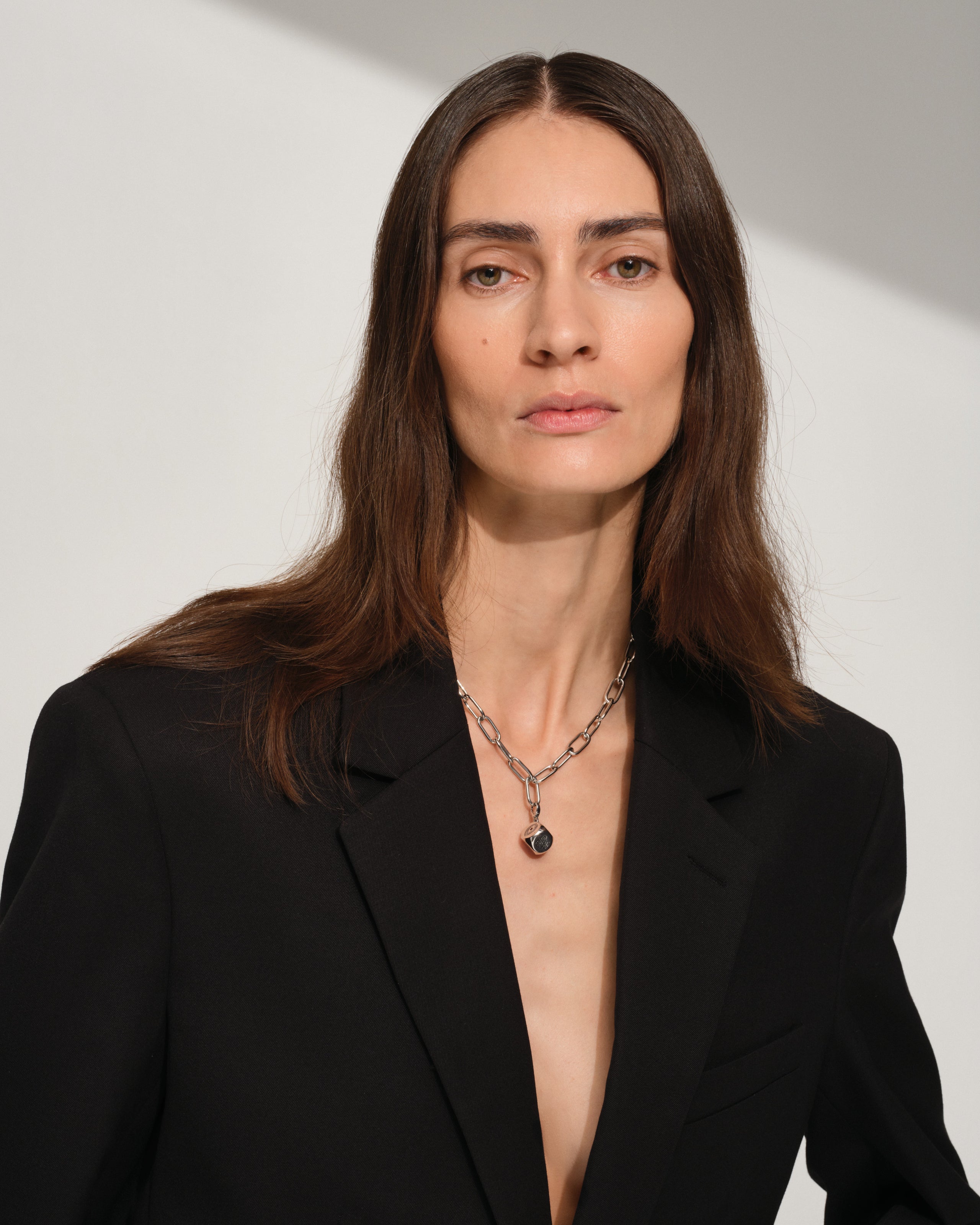 Woman wearing a black blazer with a 925 sterling silver necklace with a sterling silver dice charm against a plain background