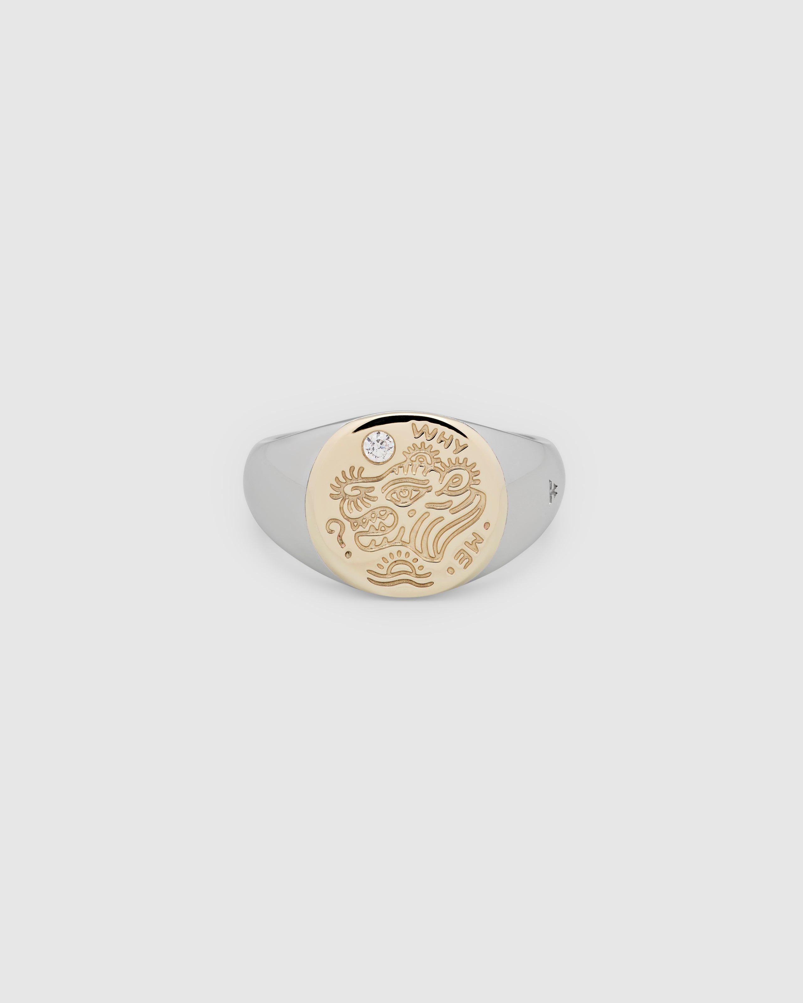 A small, round gold and 925 sterling silver signet ring for men and women, featuring an engraved custom motif from Gey Le Tatooer and a hand-set, lab-grown diamond on the surface.