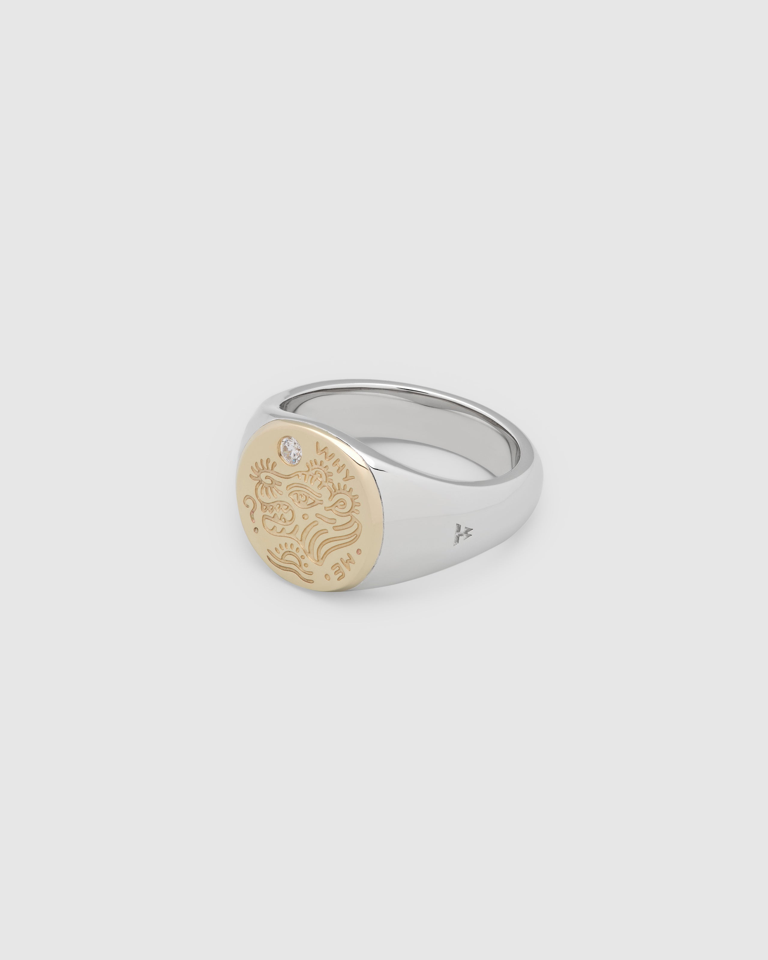A small, round gold and 925 sterling silver signet ring for men and women, featuring an engraved custom motif from Gey Le Tatooer and a hand-set, lab-grown diamond on the surface.