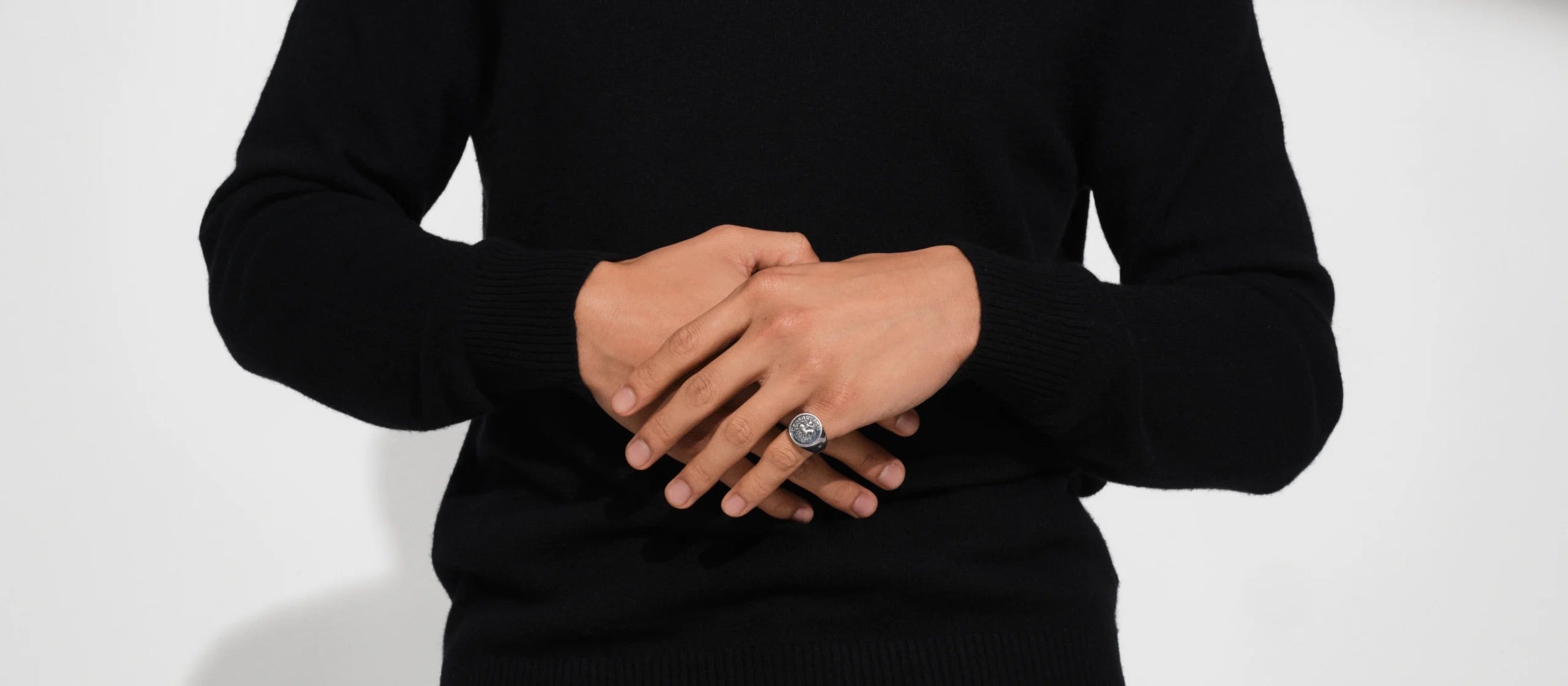 Person in a black long-sleeve top wearing a signet ring on their pinky finger.
