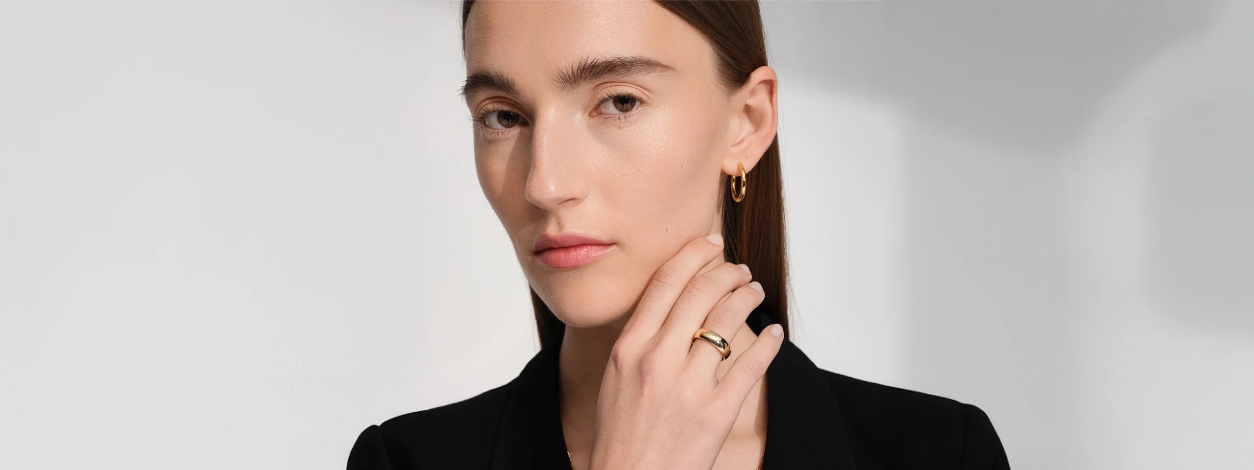 Woman in a black jacket wearing a gold ring and matching gold earrings.