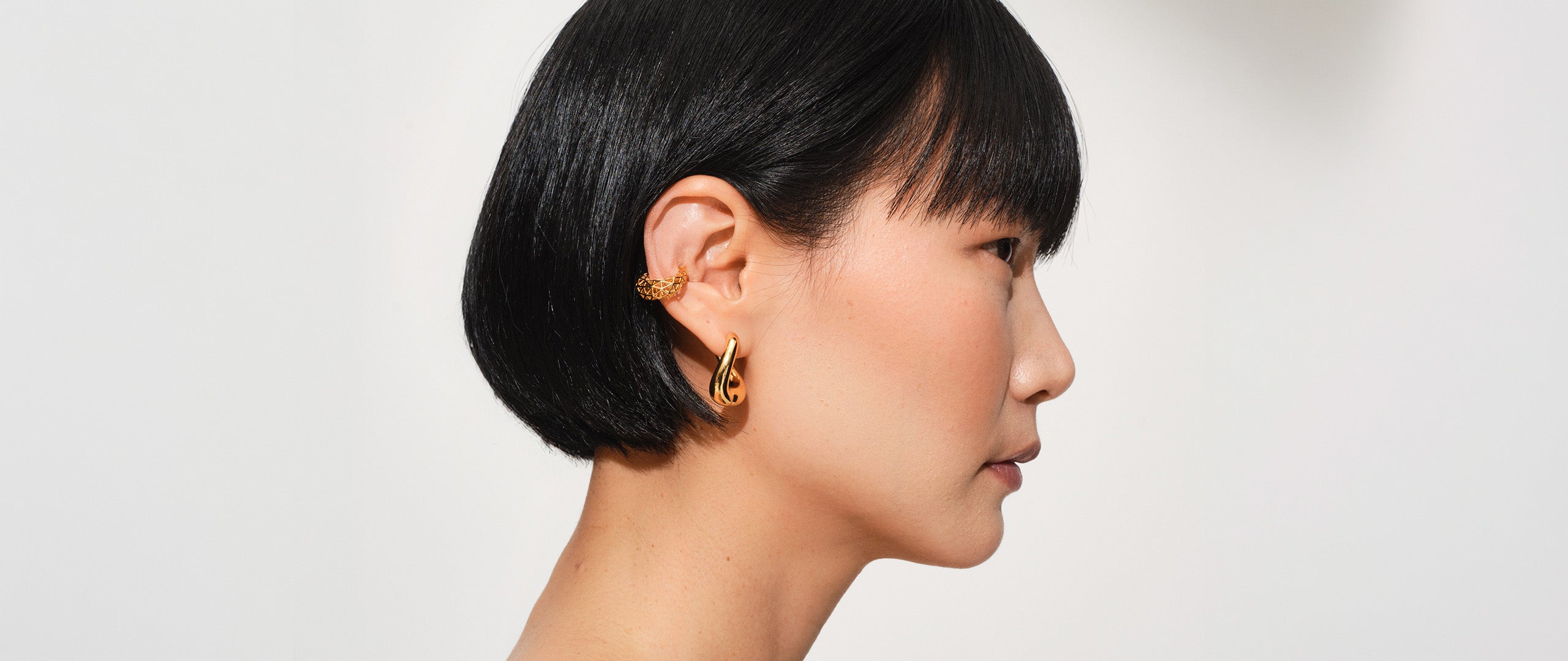 Side profile of a woman with short dark hair wearing a gold hoop earring and god ear cuff.
