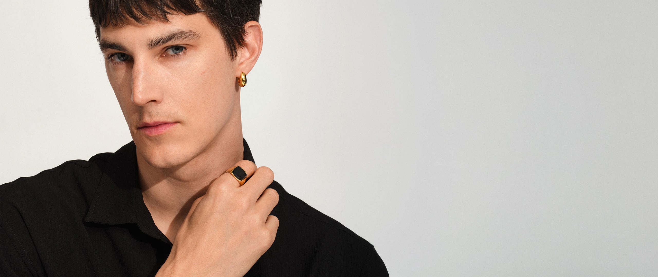 Man in a black shirt wearing a gold signet ring with a dark stone setting.
