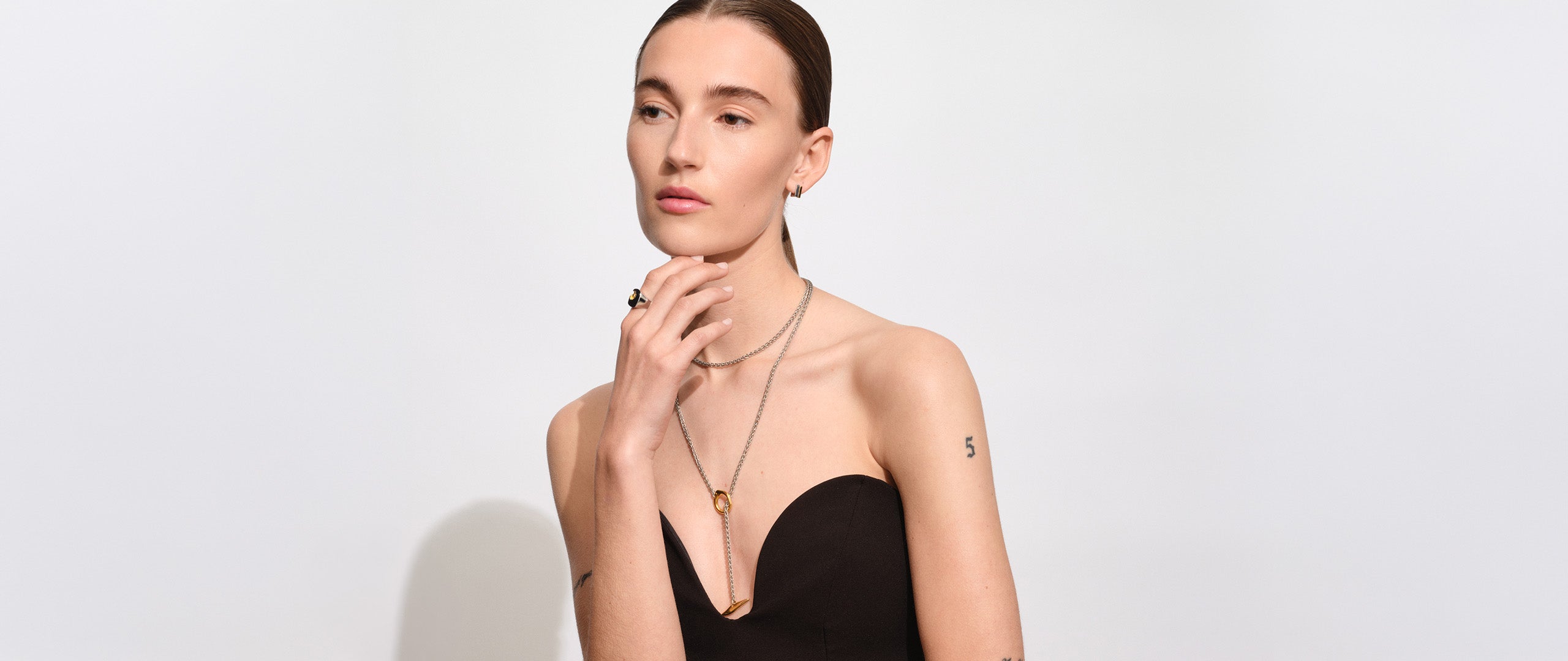 Portrait of a woman with slicked-back hair wearing layered gold and silver necklaces and matching mixed-metal rings.