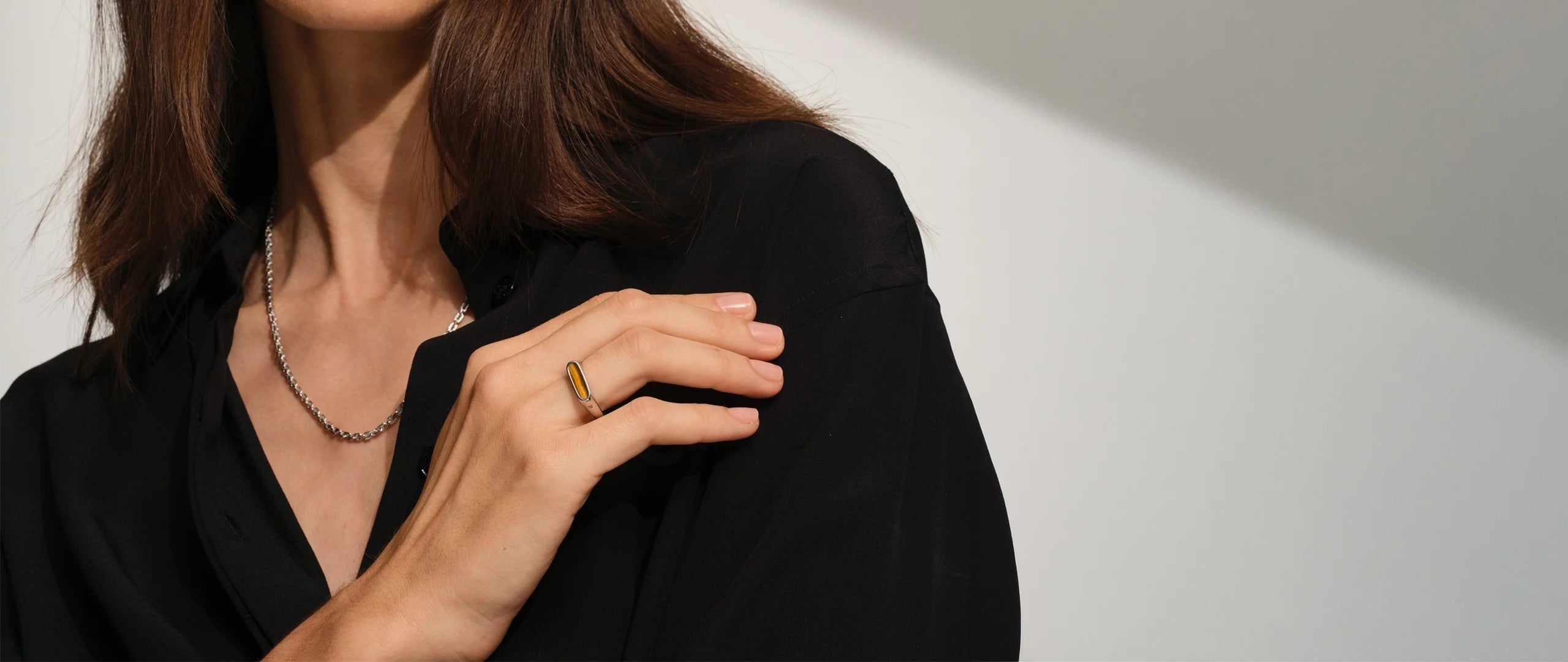 Woman in a black outfit wearing a gold tiger eye ring and a fine silver chain necklace.