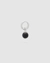 A silver huggie hoop earring with a dangling black spherical bead charm, shown against a solid light gray background.