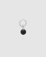 A silver huggie hoop earring with a dangling black spherical bead charm, shown against a solid light gray background.