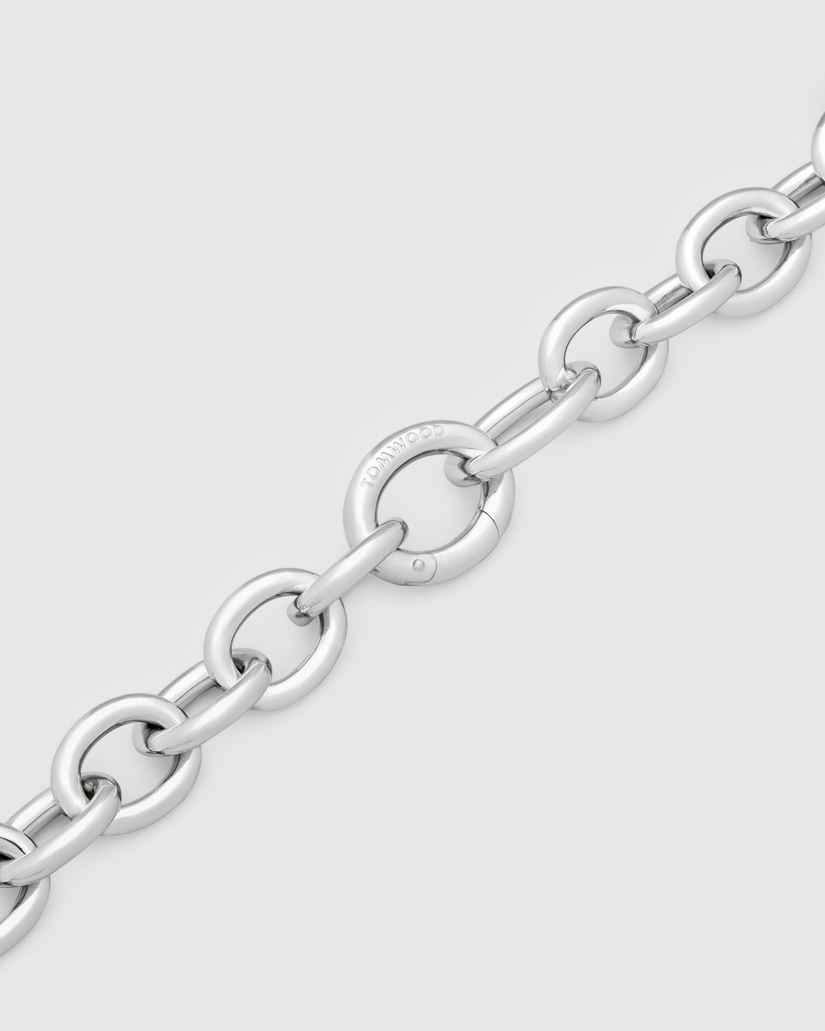 A close-up of a polished silver bracelet with interlocking oval links, including one clearly engraved with the brand name 'TOMWOOD' on a light gray background.