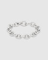 A polished silver chain link bracelet with a flat, wide oval link design, displayed on a light gray background.