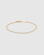 A delicate gold chain bracelet with a lobster clasp and a small rectangular engraved logo tag, displayed on a light gray background.