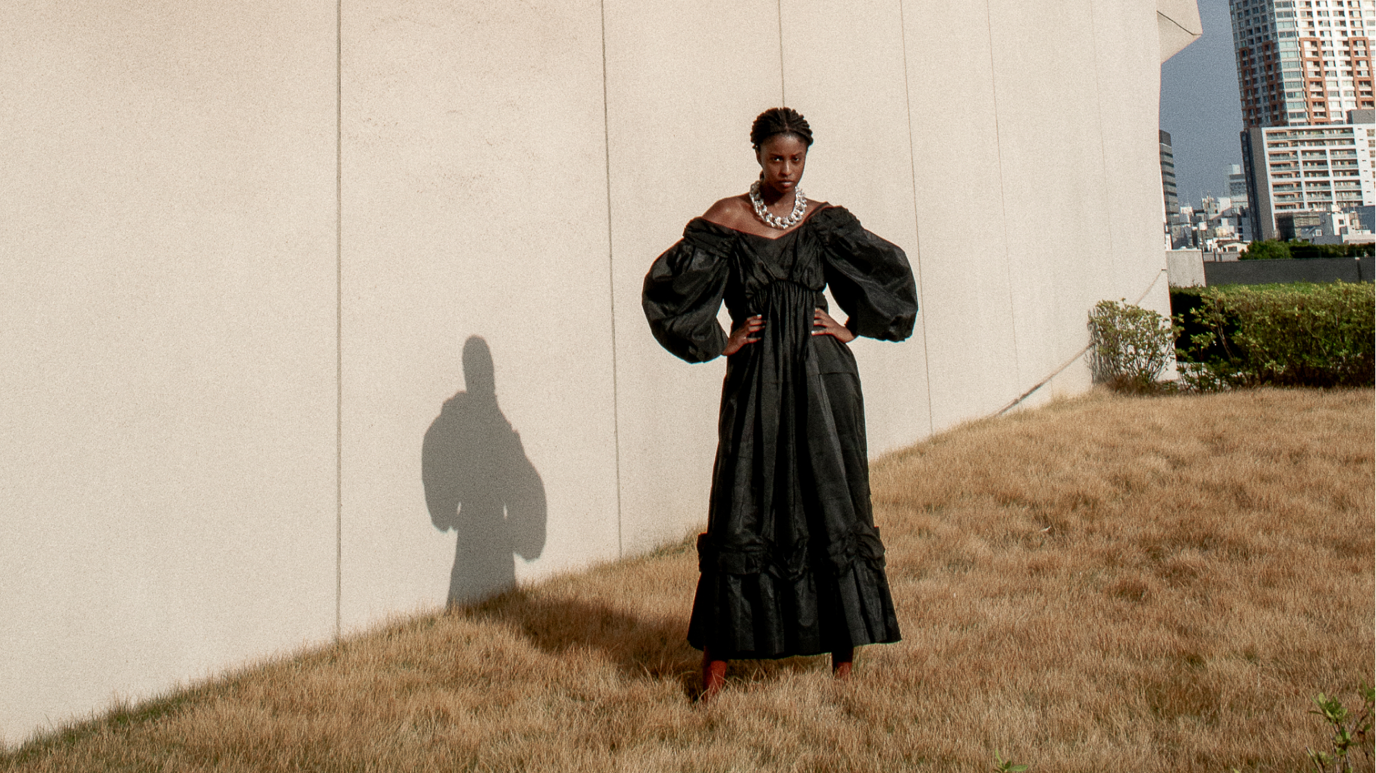Woman in a black dress standing against a beige wall with a cityscape in the background