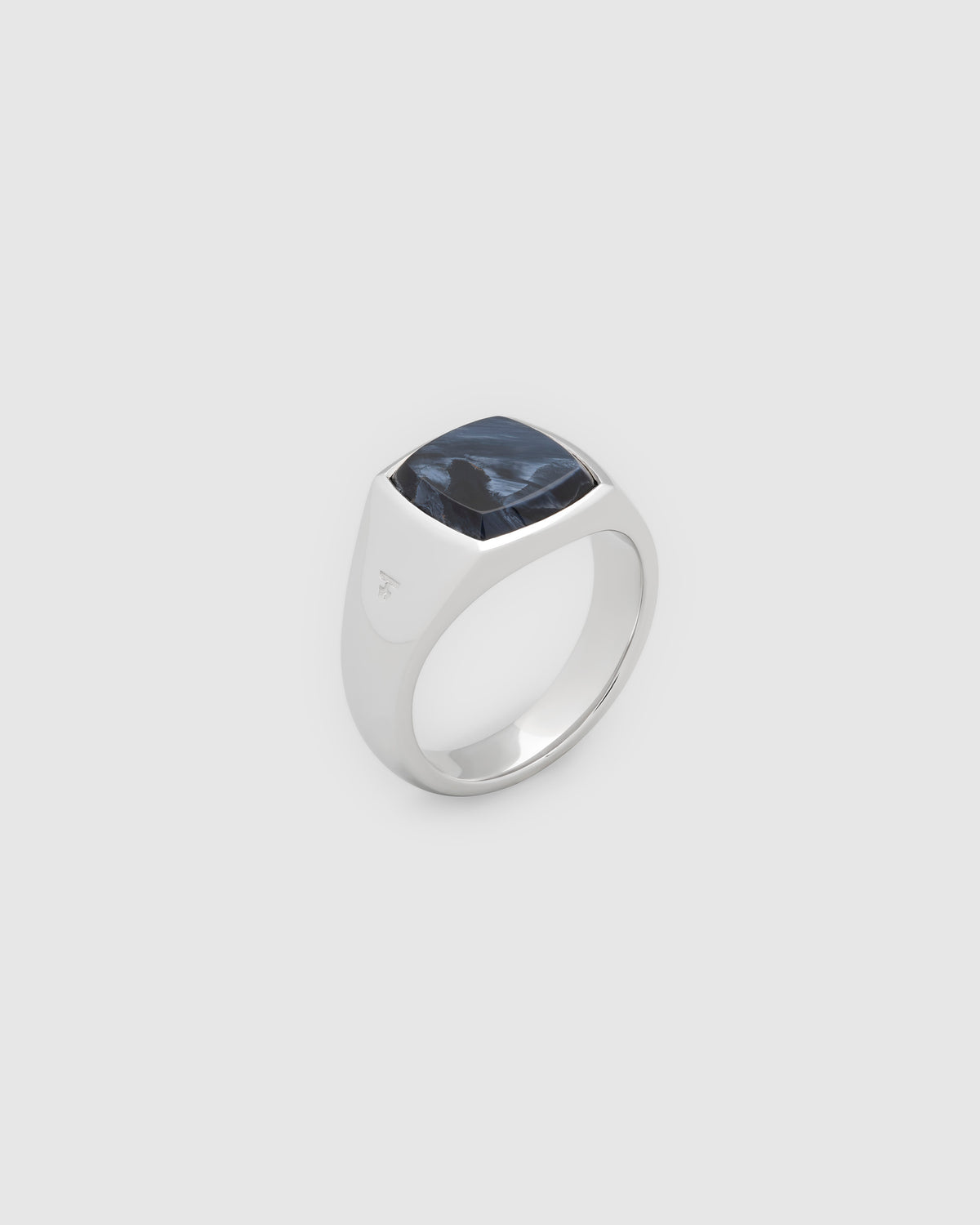 A silver signet ring featuring a square-cut dark blue pietersite gemstone, shown on a neutral light gray background.