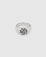 A small, round signet 925 sterling silver ring for men and women, featuring an engraved custom motif by Guy Le Tatooer and a hand-set, deep red garnet stone on the surface.