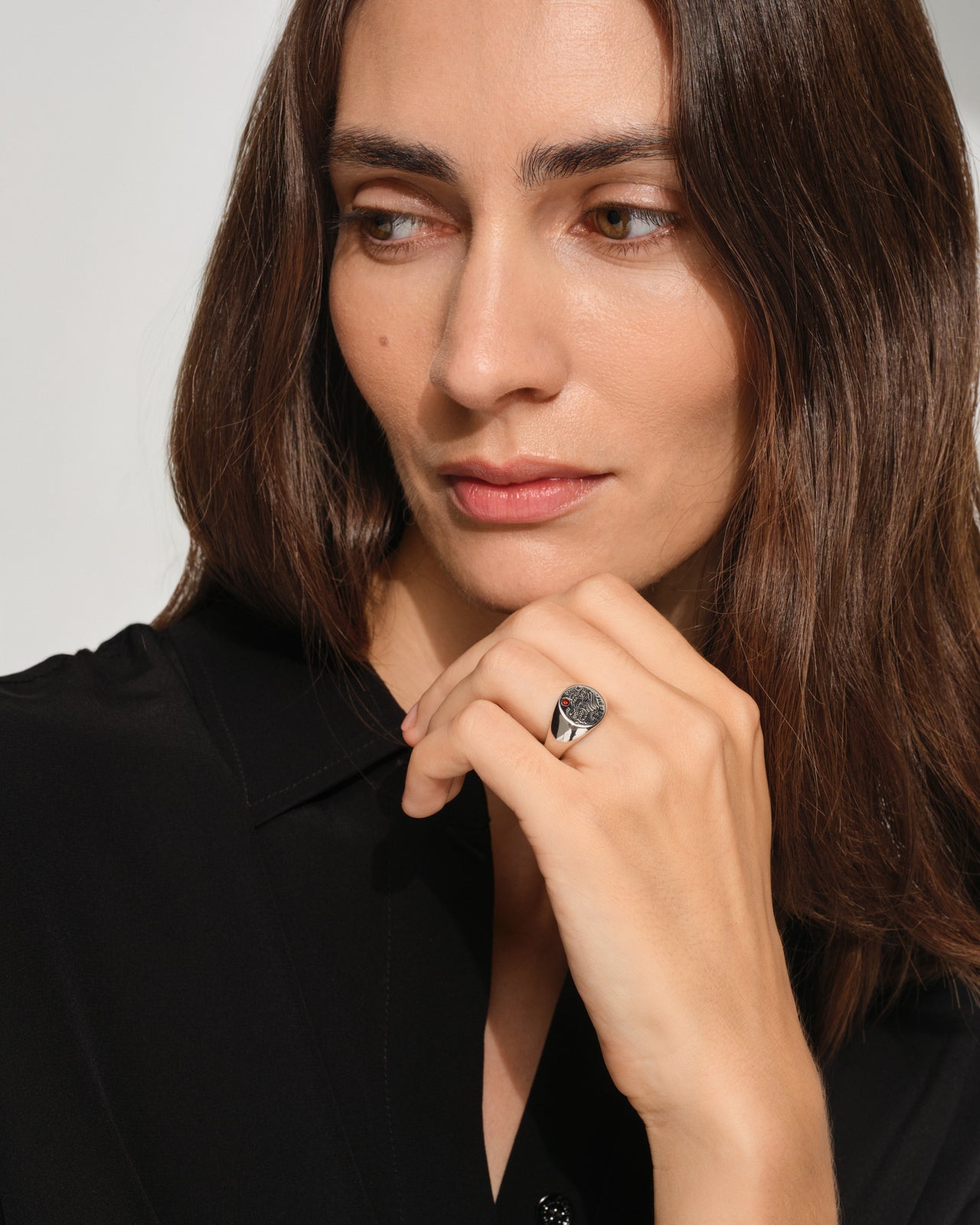 woman wearing a small, round signet 925 sterling silver ring for men and women, featuring an engraved custom motif by Guy Le Tatooer and a hand-set, deep red garnet stone on the surface.