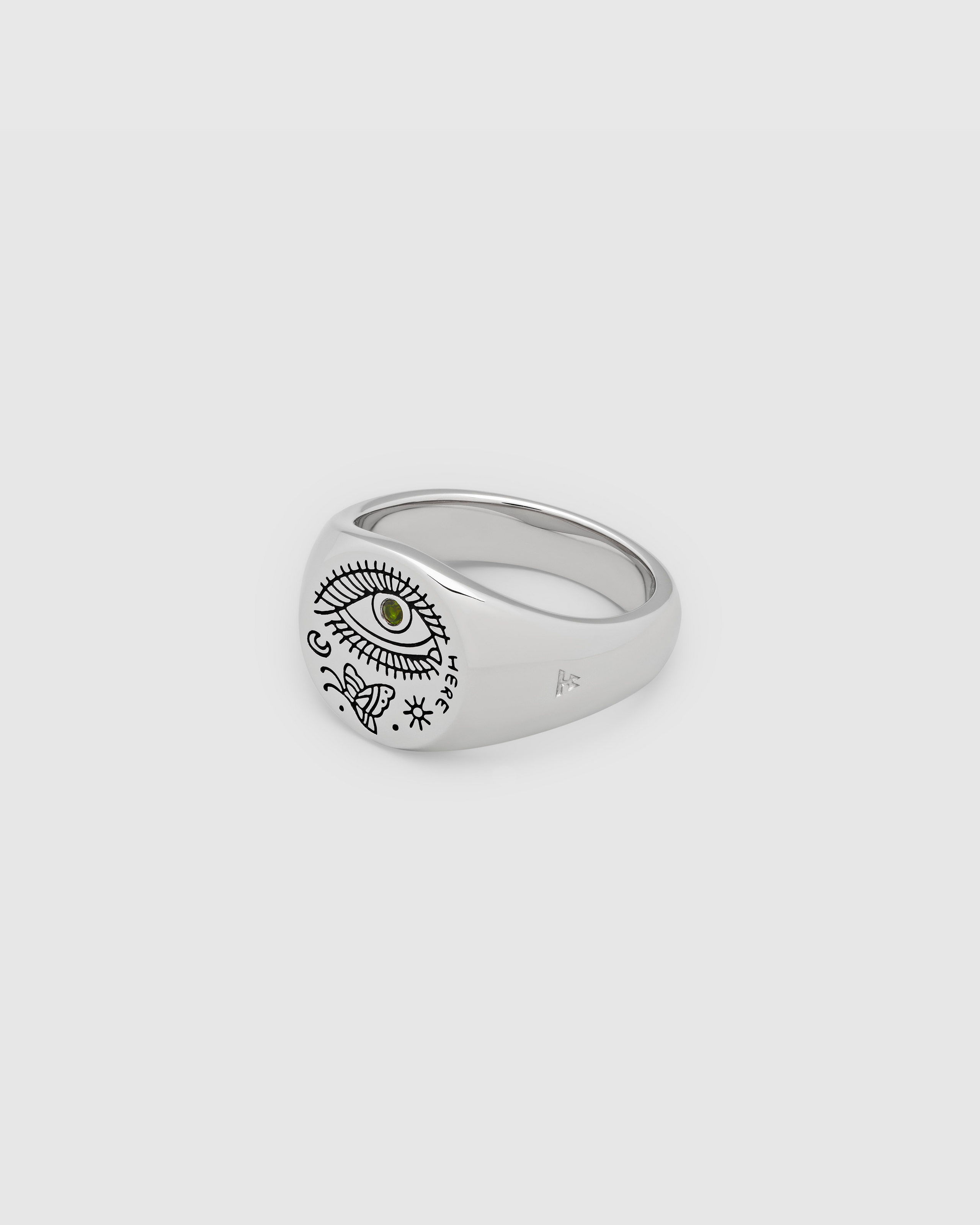A small, round signet 925 sterling silver ring for men and women, featuring an engraved custom motif by Guy Le Tatooer and a hand-set, deep green tourmaline stone on the surface.