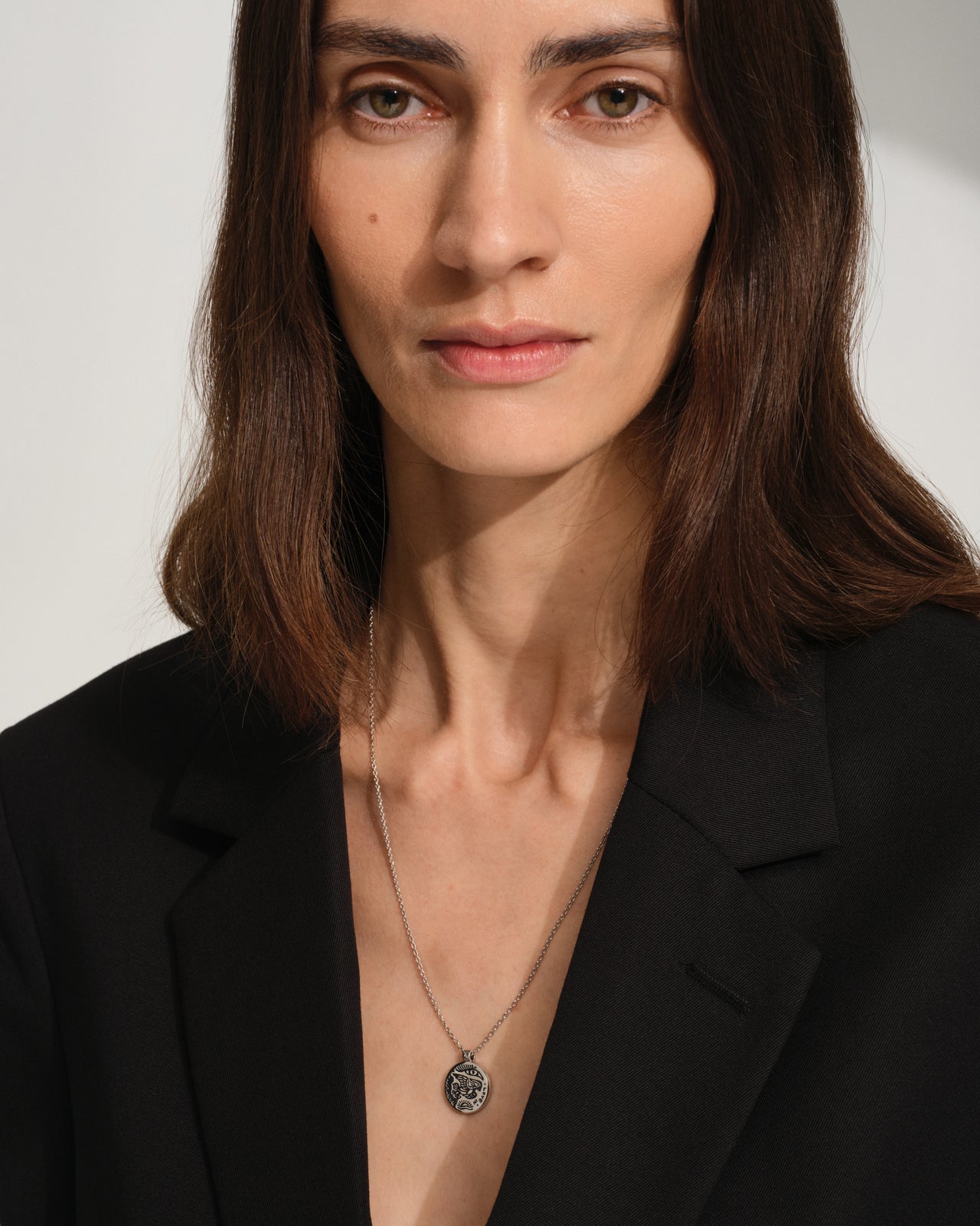 Woman wearing a black blazer and 925 sterling sivler necklace with a silver pendant on a plain background