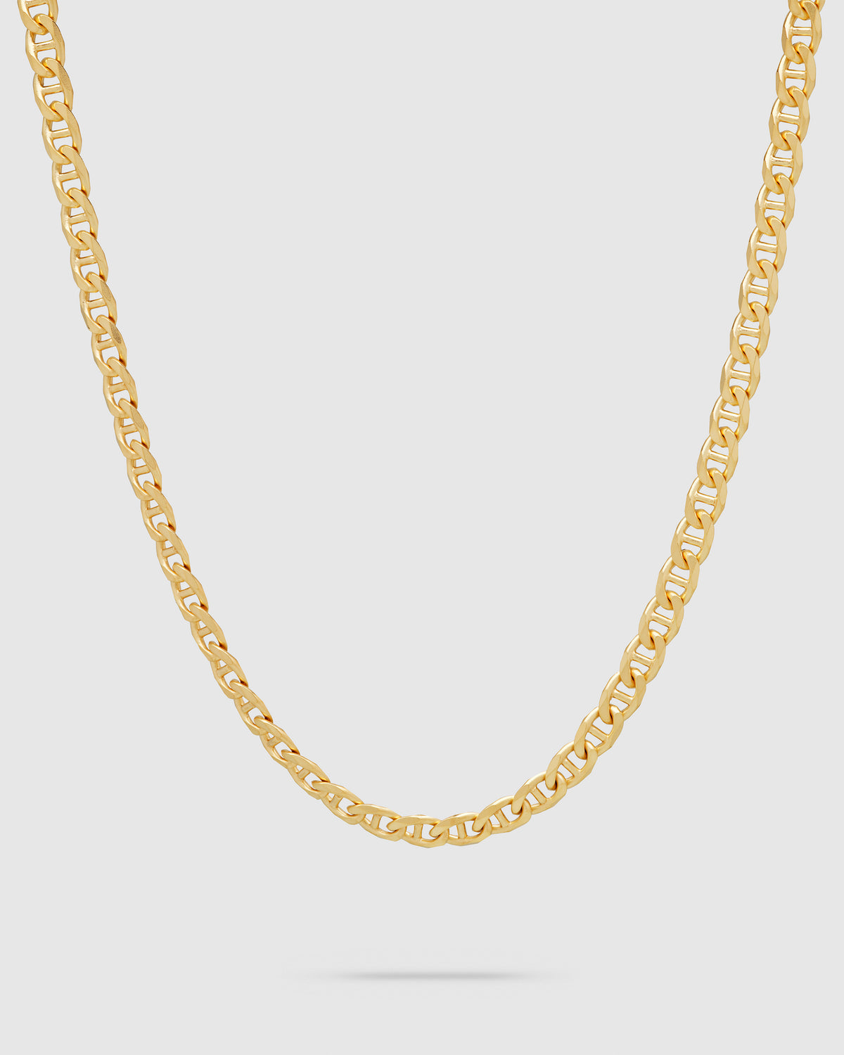 A gold curbed jude chain necklace displayed in a curved shape against a light gray background.