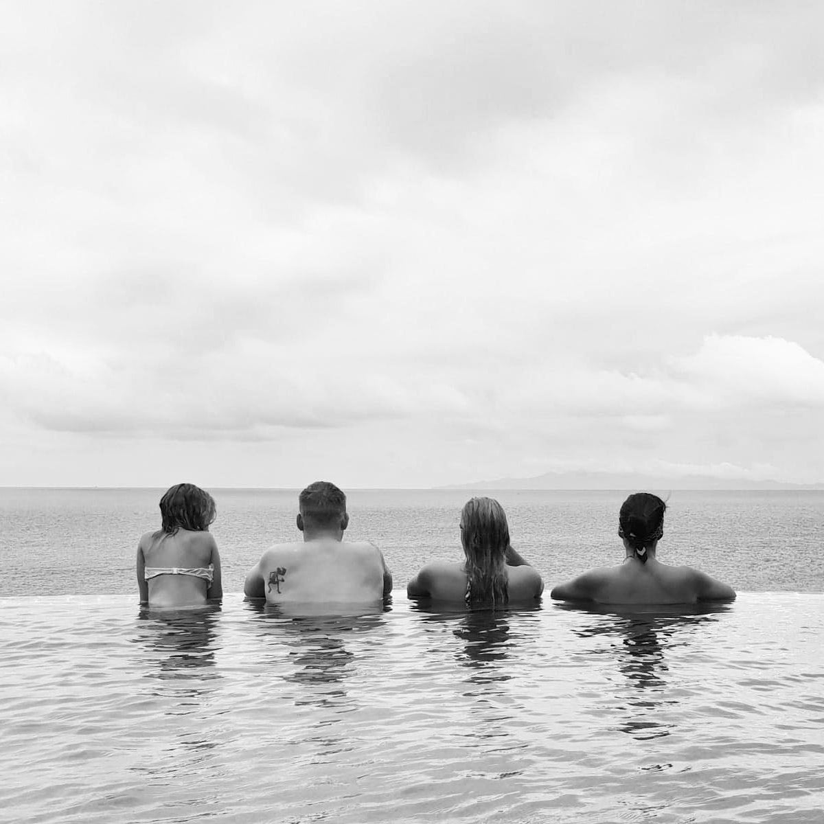 Four people sitting in water looking out at a cloudy sky