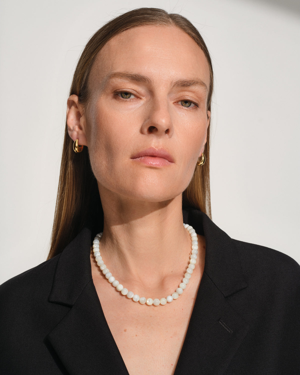 Tom Wood Cove Necklace White MOP - A woman wearing a white pearl necklace and small gold hoop earrings.